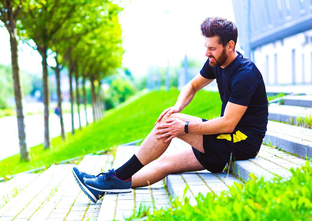 Coureur assis avec la main posée sur son genou douloureux